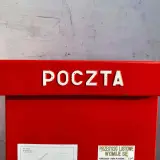 Czerwona skrzynka pocztowa z napisem "POCZTA". Informacja o godzinie odbioru przesyłek listowych: 14:00. Dowiedz się, ile kosztuje przelew na poczcie.