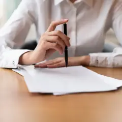 Dłoń z długopisem nad stosem papierów, przygotowująca skargę na kuriera InPost.