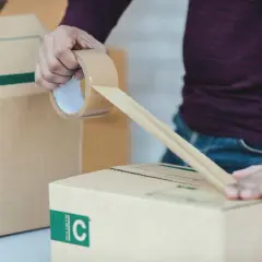 Osoba zakleja taśmą kartonowe pudło. To część procesu przygotowania przesyłki, który może być związany z odprawą celną.