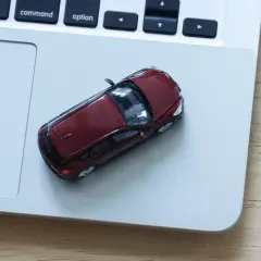Czerwony samochodzik na laptopie. Zastanawiasz się, ile kosztuje wystawienie samochodu na OLX?