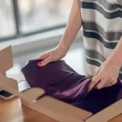 Kupujesz na Vinted i zastanawiasz się, co jeśli sprzedający nie wyśle paczki? Kobieta pakuje bordową sukienkę do kartonu.
