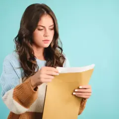 Młoda kobieta otwiera kopertę z listem poleconym, zastanawiając się, od kogo jest.