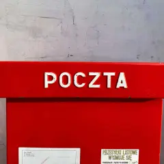Czerwona skrzynka pocztowa z napisem "POCZTA". Informacja o godzinie odbioru przesyłek listowych: 14:00. Dowiedz się, ile kosztuje przelew na poczcie.