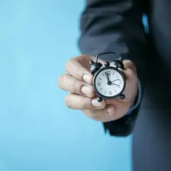 Dłoń trzyma budzik. Czas ucieka, a Kaczmarski Group oszuści wciąż działają.