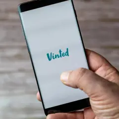Dłoń trzyma smartfon z logo Vinted. Planuję odbiór osobisty zakupionych ubrań.