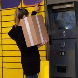 Kobieta z paczką przy paczkomacie. Dowiedz się, jak nadać paczkę w paczkomacie, korzystając z intuicyjnego panelu.