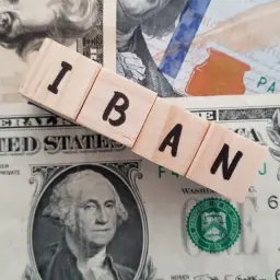 Drewniane klocki z literami IBAN leżą na banknotach dolarowych. IBAN to międzynarodowy numer rachunku bankowego.