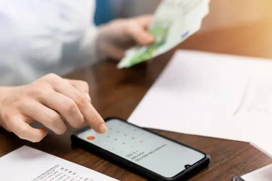 Ręka liczy pieniądze na kalkulatorze w telefonie. Czy to próba uniknięcia komornika, czy po prostu zarządzanie budżetem? Konto zen i komornik to stresujące połączenie.