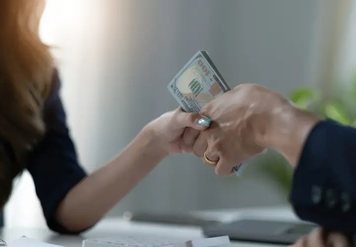 Dwie osoby przekazują sobie plik banknotów. To może być pożyczka od osoby prywatnej, która pomoże w nagłej potrzebie.
