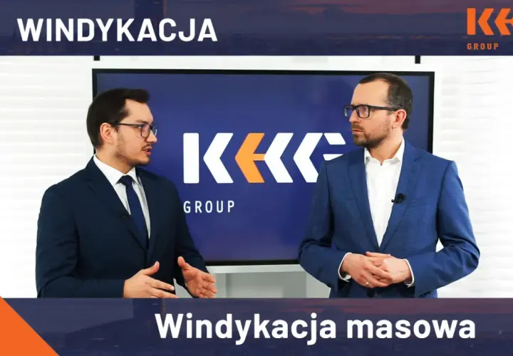 Dwóch mężczyzn w garniturach stoi przed ekranem z logo KK GROUP.