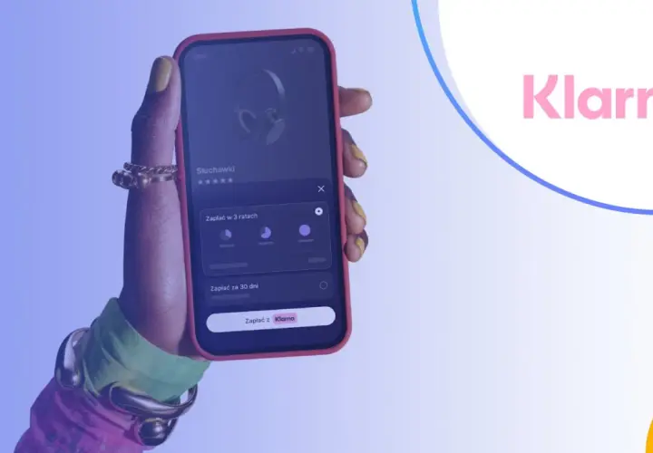 Dłoń trzyma smartfon z aplikacją Klarna, umożliwiającą zakup słuchawek na raty.