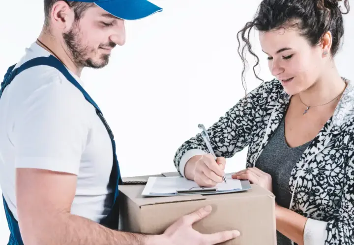 Kurier w niebieskim uniformie podaje paczkę kobiecie, która podpisuje dokumenty.