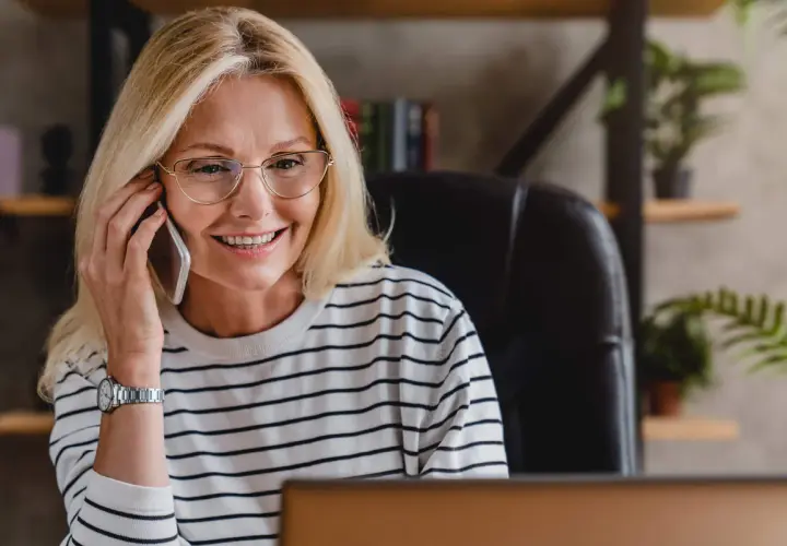 Uśmiechnięta blondynka w okularach rozmawia przez telefon, szukając pożyczki na telefon od zaraz.