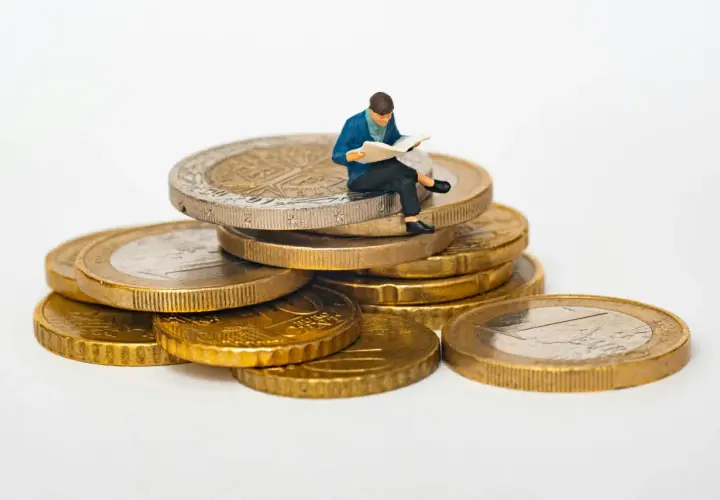 Figurka siedząca na stosie monet euro, czytająca gazetę. Symbolizuje eurocent pożyczki do domu.