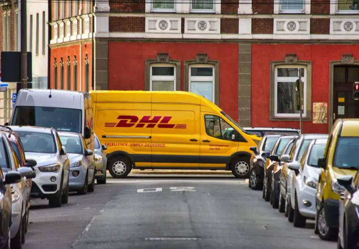 Żółta furgonetka DHL zaparkowana na ulicy, obok inne samochody. Może być potrzebny protokół szkody.