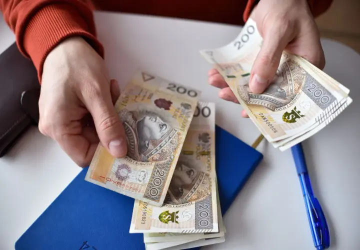 Ręce liczą banknoty 200 zł. Obok niebieski notatnik i długopis. Może to przygotowanie do złożenia wniosku o rozłożenie na raty ZUS uzasadnienie przykład.