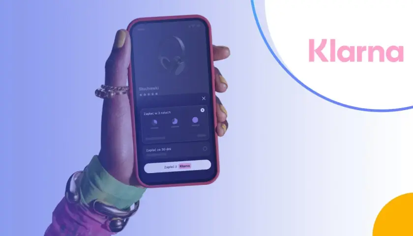 Dłoń trzymająca telefon z aplikacją Klarna, pokazującą opcje płatności za słuchawki.