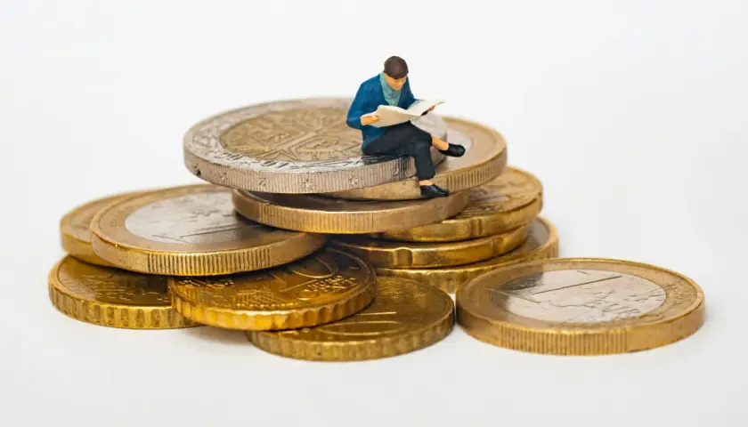 Figurka siedząca na stosie monet euro, czytająca gazetę. Symbolizuje eurocent pożyczki do domu.