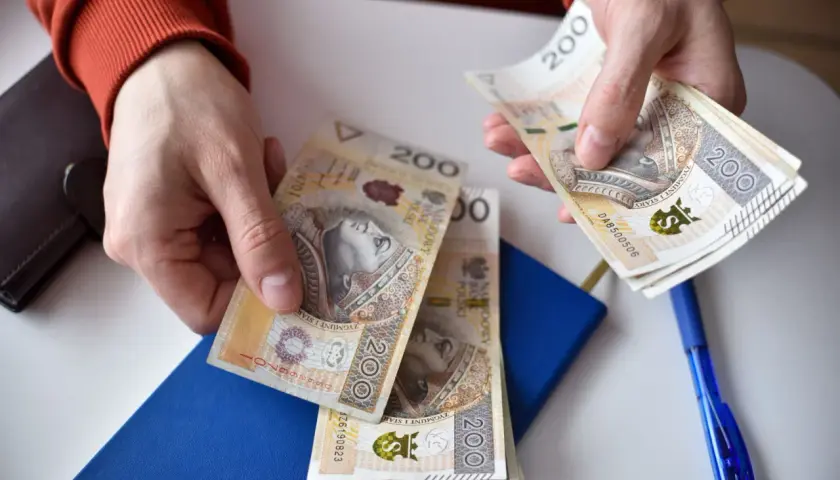 Ręce liczą banknoty 200 zł. Obok niebieski notatnik i długopis. Może to przygotowanie do złożenia wniosku o rozłożenie na raty ZUS uzasadnienie przykład.