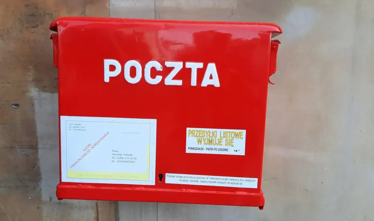 Czerwona skrzynka pocztowa z napisem "POCZTA". Obok etykieta z adresem i informacją, czy żona może odebrać list polecony z sądu.