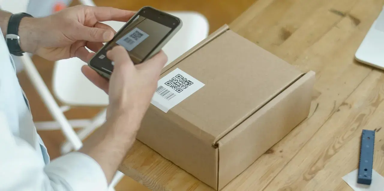 Ręce skanują kod QR na paczce, przygotowując ją do wysyłki w ramach dropshippingu.