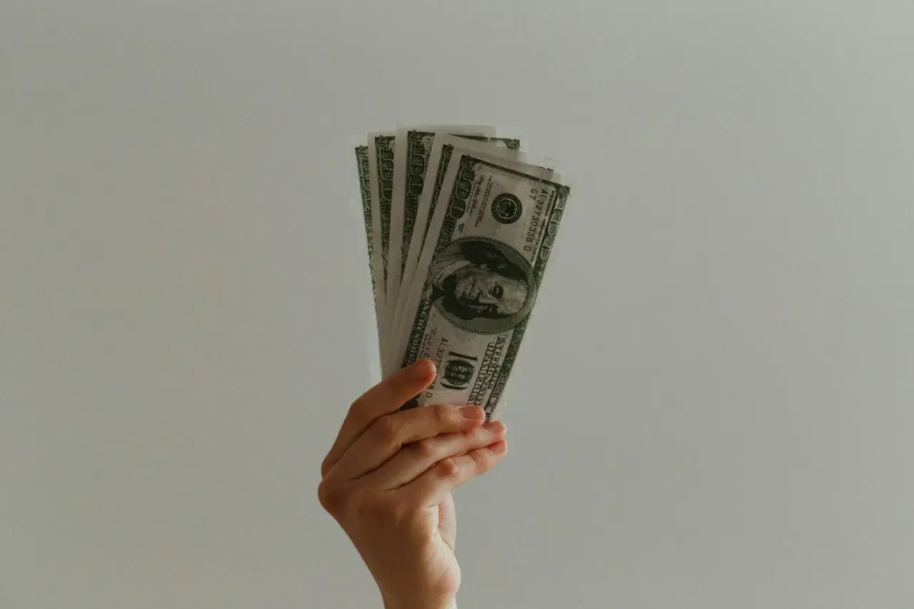 Dłoń trzyma banknoty 100 dolarów, symbolizujące umowę pożyczki.
